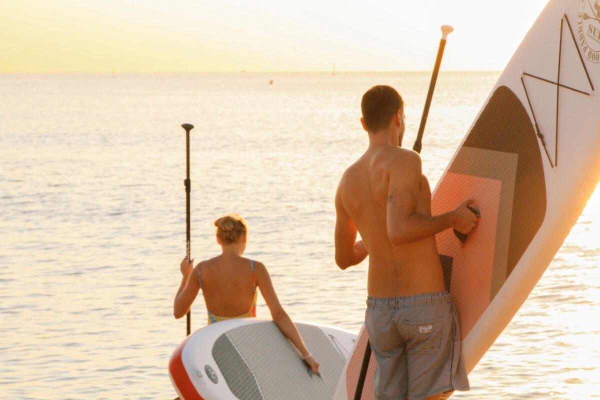 man and woman holding paddleboards