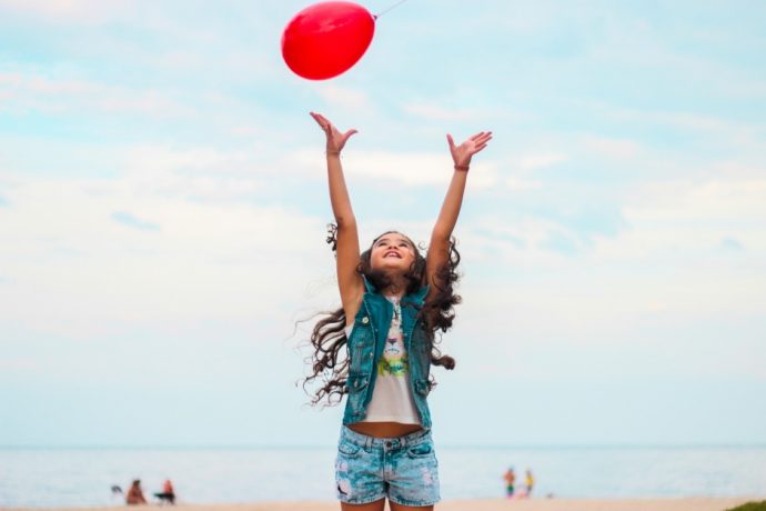 Little girl throwing a balloon in the air on the beach